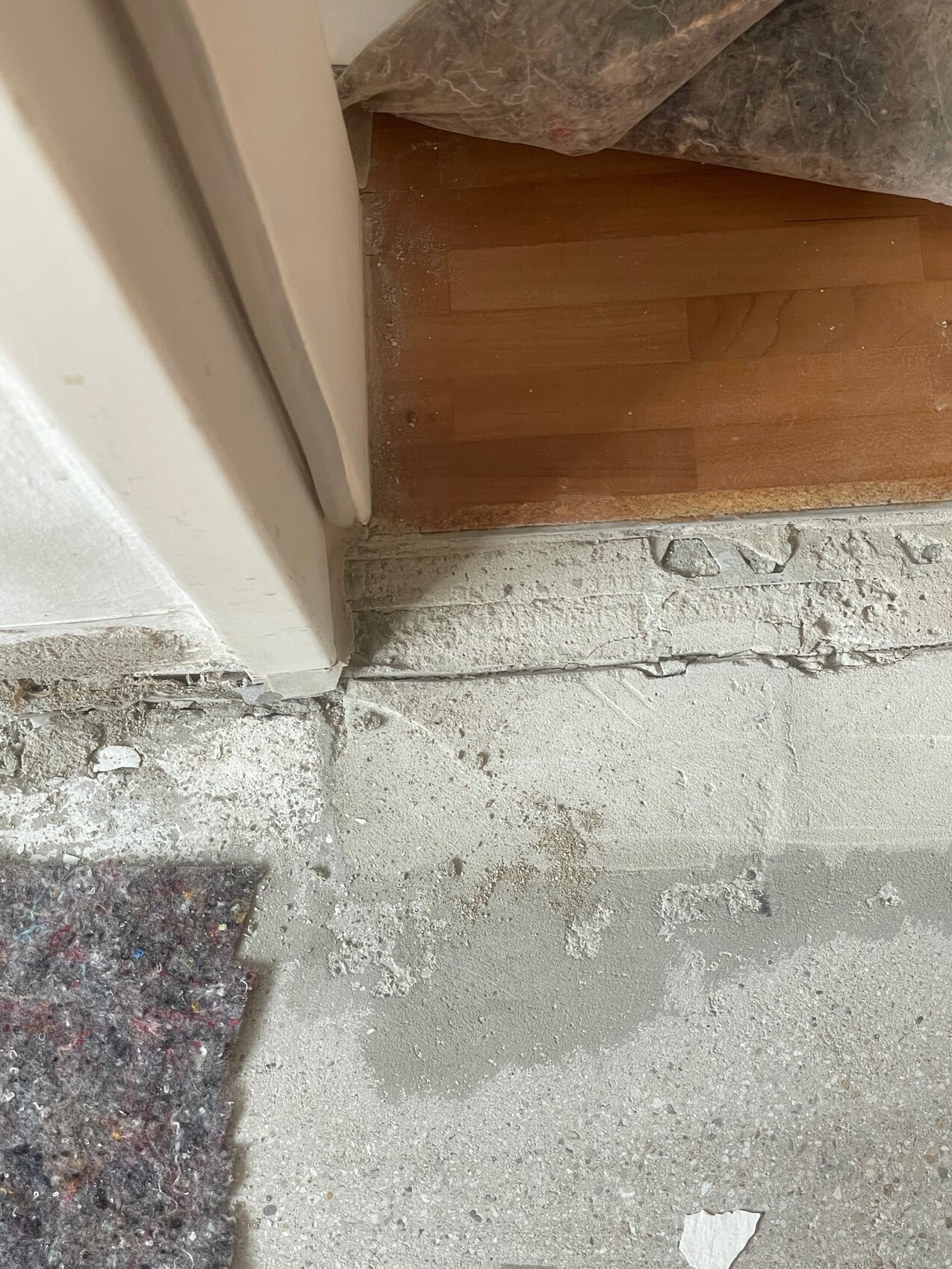 Türschwelle: Holzboden hinter Tür, staubiger Betonboden und Baureste vor dem Übergang.