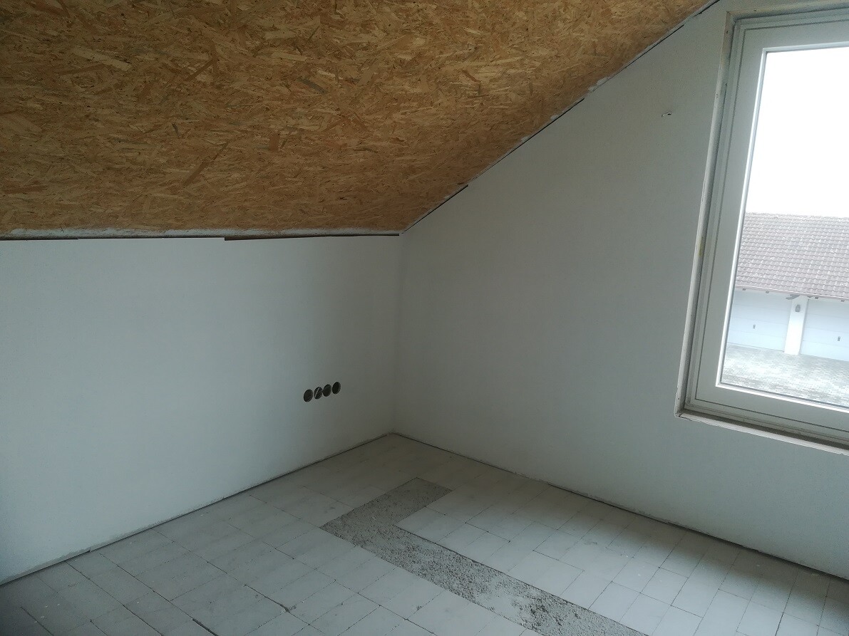 Leerraum im Dachgeschoss mit schräger OSB-Decke, Fenster rechts, weiße Wände, fünf runde Steckdosen.