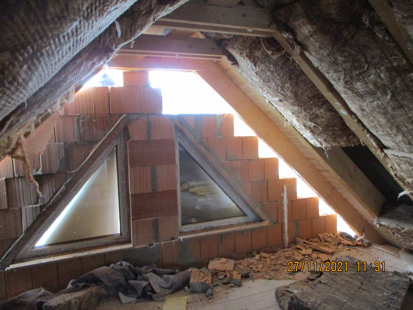 Dachboden-Rohbau mit roten Ziegelwänden, Dreiecksfenstern, Holzbalken und Geröll.