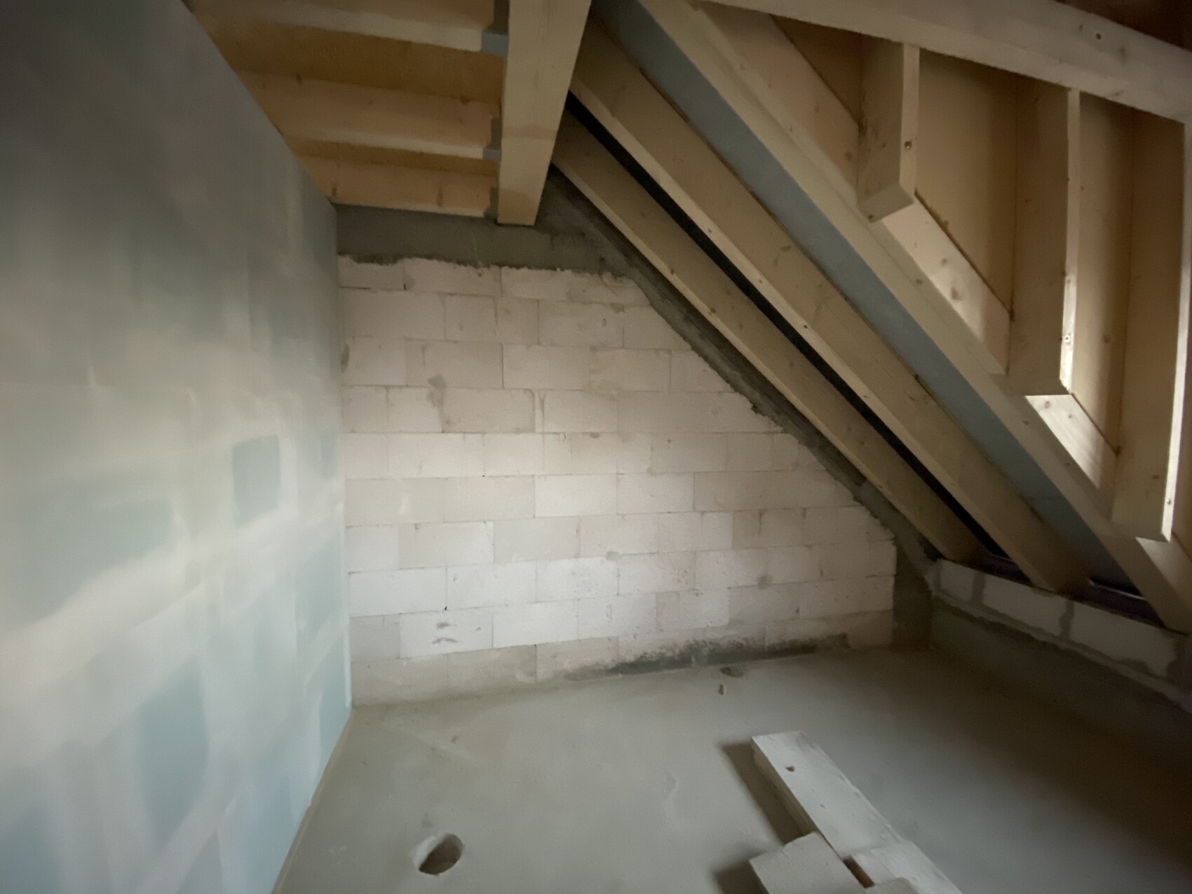 Unfertiger Dachboden: sichtbare Holzbalken, weiße Steinblöcke und unbehandelter Betonboden.