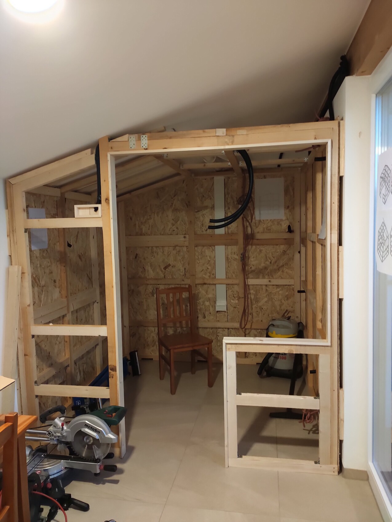 Unfertiger Innenraum mit Holzrahmen, OSB-Platten, Stuhl und Werkzeugen.