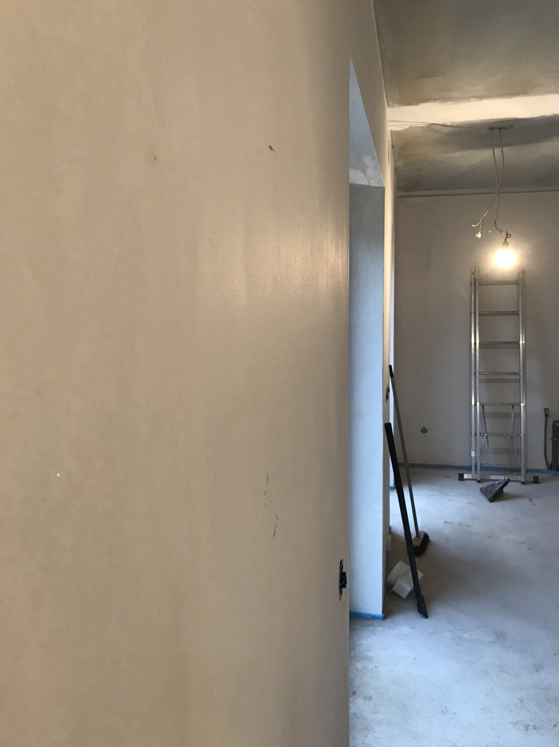 Innenraum einer Baustelle: Metallleiter, offene Decke, hängende Glühbirne, Bauwerkzeuge.