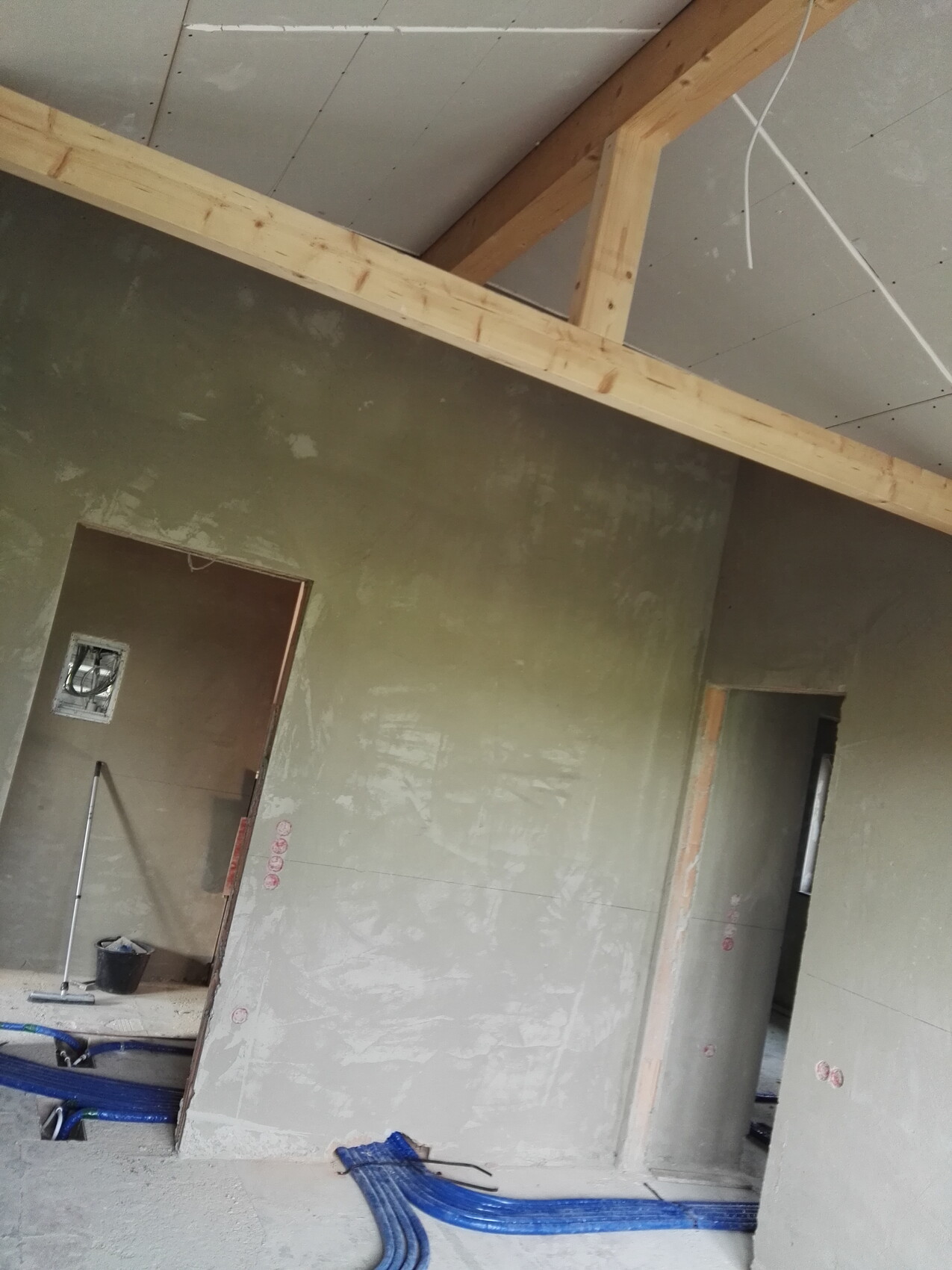 Unfertiger Innenraum einer Baustelle mit Holzbalken-Decke und blauen Kabelschläuchen am Boden.