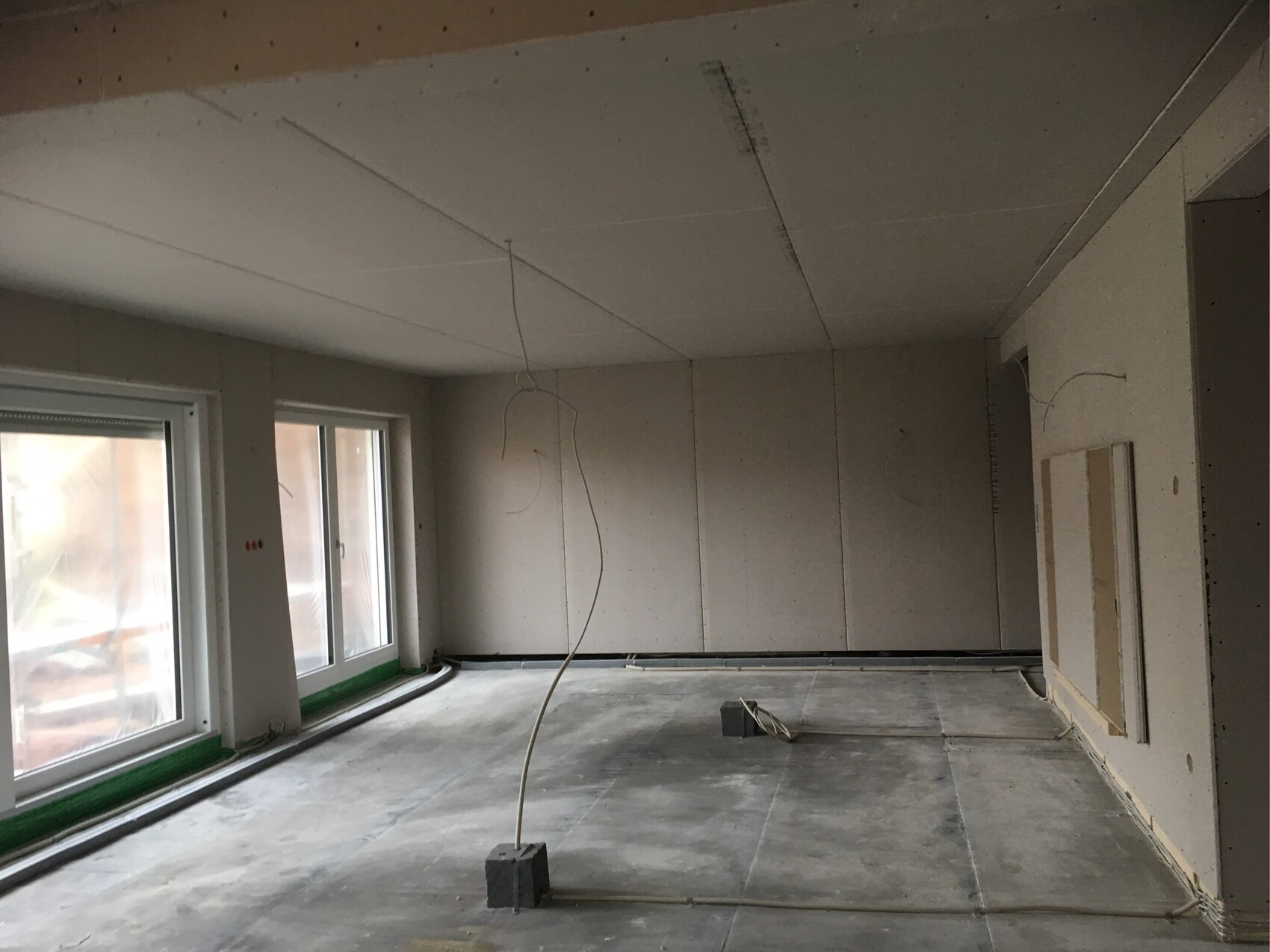 Unfertiger Innenausbau Raum mit Fenstern, Trockenbauwänden und freiliegenden Kabeln