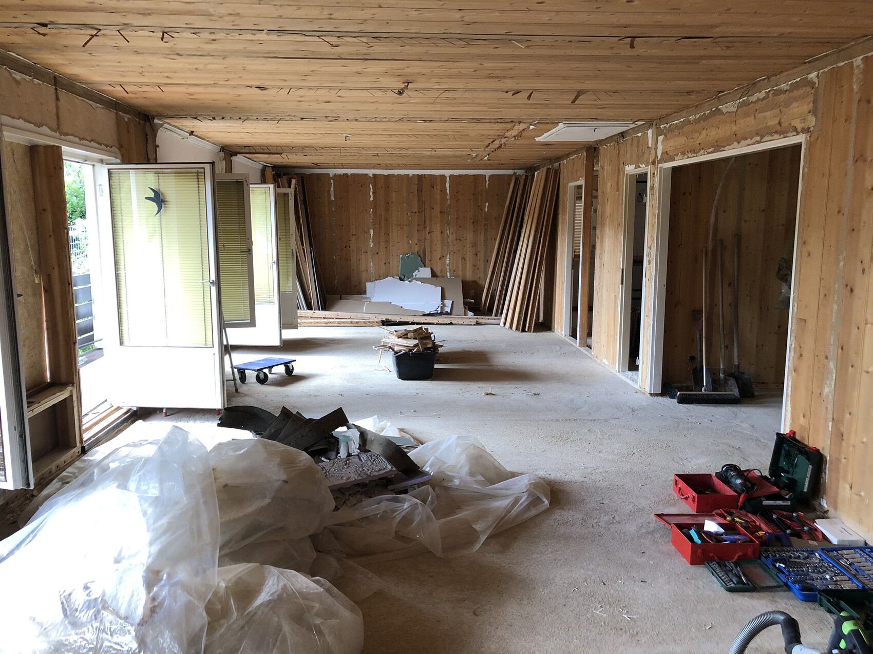 Offener Innenraum im Renovierungszustand mit Holzwänden, Bauholz, Werkzeugkiste und Plastiksäcken.
