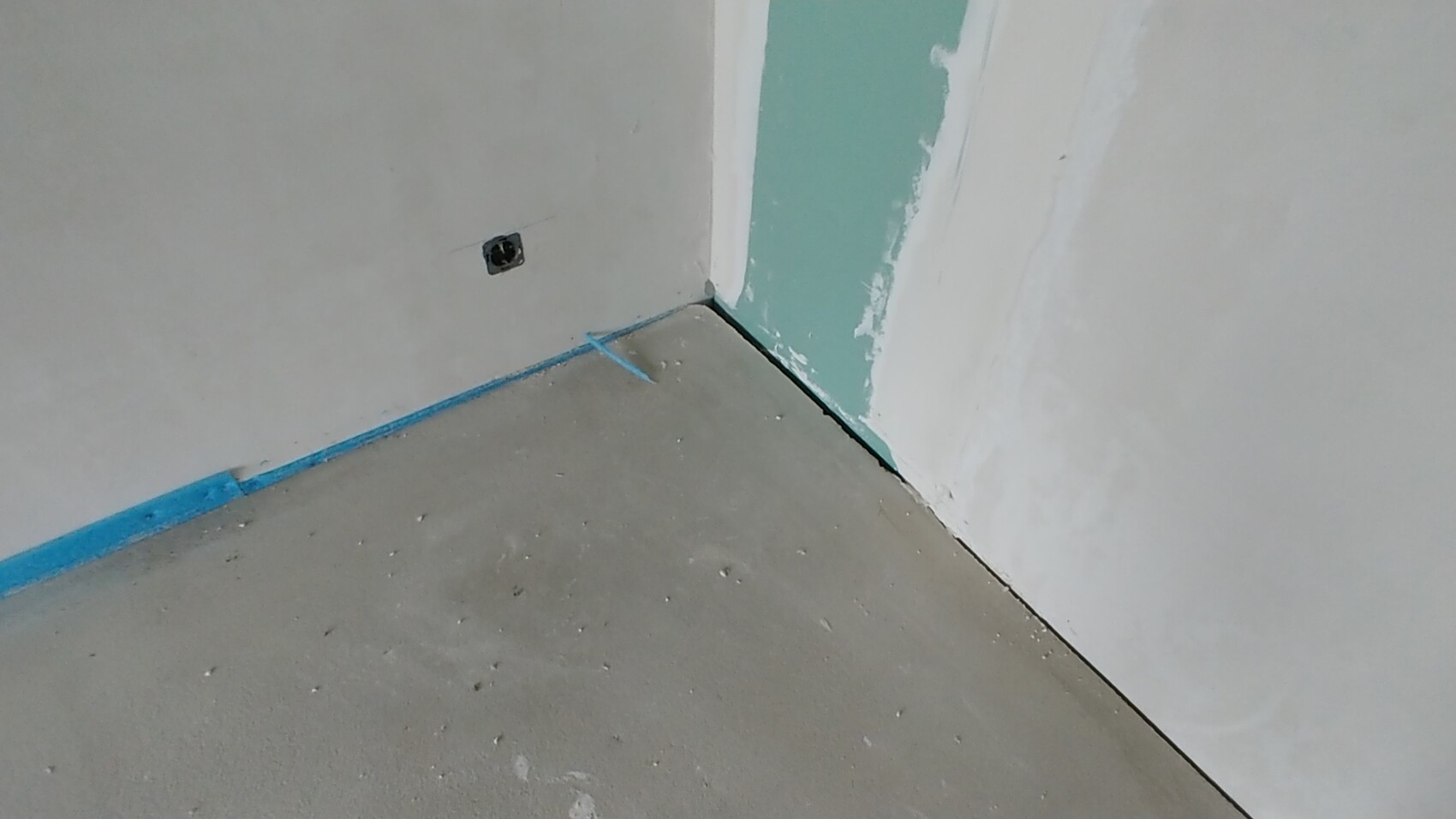 Unfertiger Innenraum im Bau mit rohen Wänden, Ecke, Boden mit blauer Abdeckkante und Steckdosenöffnung