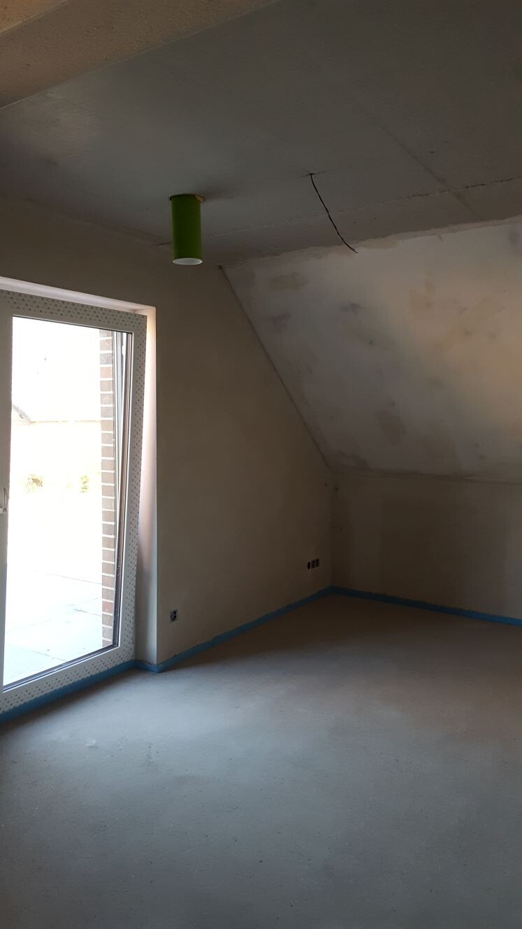 Unfertiger Innenraum im Dachgeschoss mit rohem Boden, rohen Wänden und offenem Rohr an der Decke.
