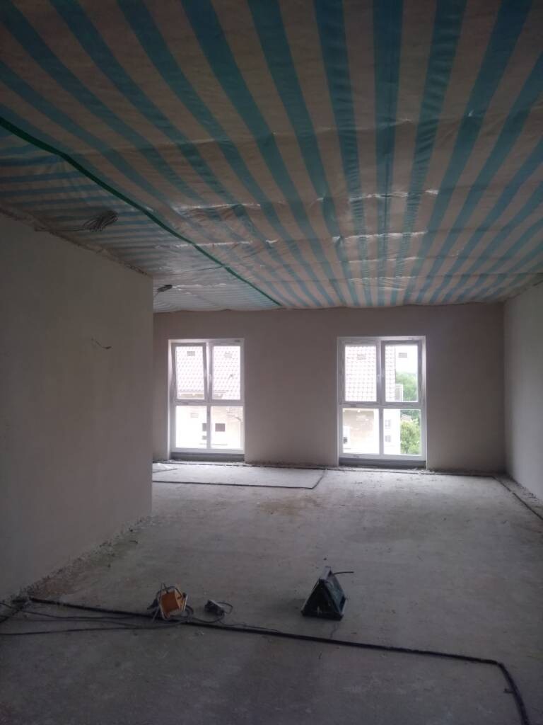 Leerer Bau-Raum mit blau-weiße Deckenfolie, zwei Fenster, Werkzeuge auf dem Boden.