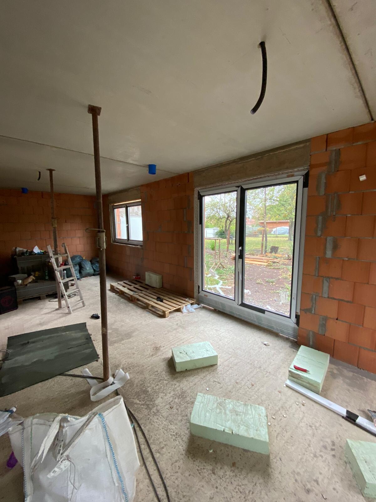 Rohbau-Raum: Innenraum mit Ziegelwänden, Fensterfront, Bauwerkzeugen, Styropor-Dämmplatten.