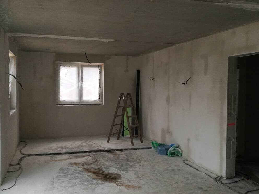 Unfertiger Innenraum einer Baustelle: Leiter, Kabel am Boden, Fenster mit Folie, Baumaterialien.