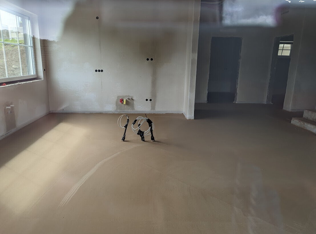 Unfertiges Zimmer mit freiliegenden Kabeln auf dem Boden, Wandöffnungen und Fenster links.