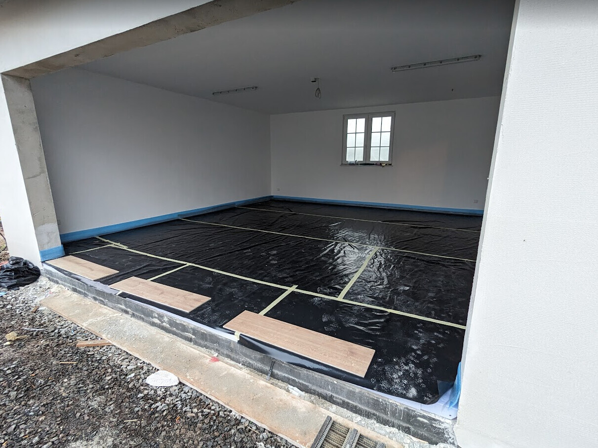 Renovierender Innenraum mit schwarzer Bodenschutzfolie, gelbem Tape, Fenster im Hintergrund.