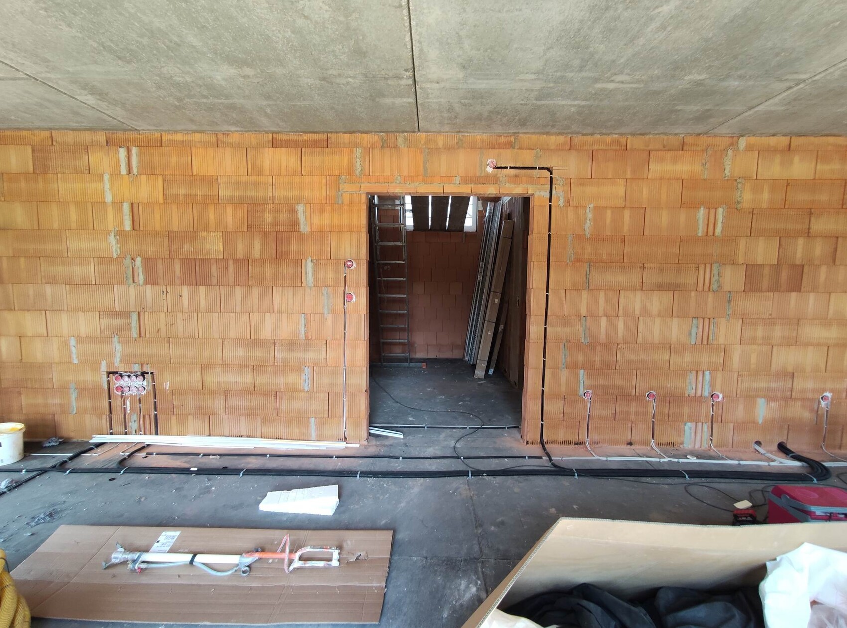Baustelle: unverputzte Backsteinwand, offener Durchgang, Leiter, Kabel und Baumaterial am Boden.