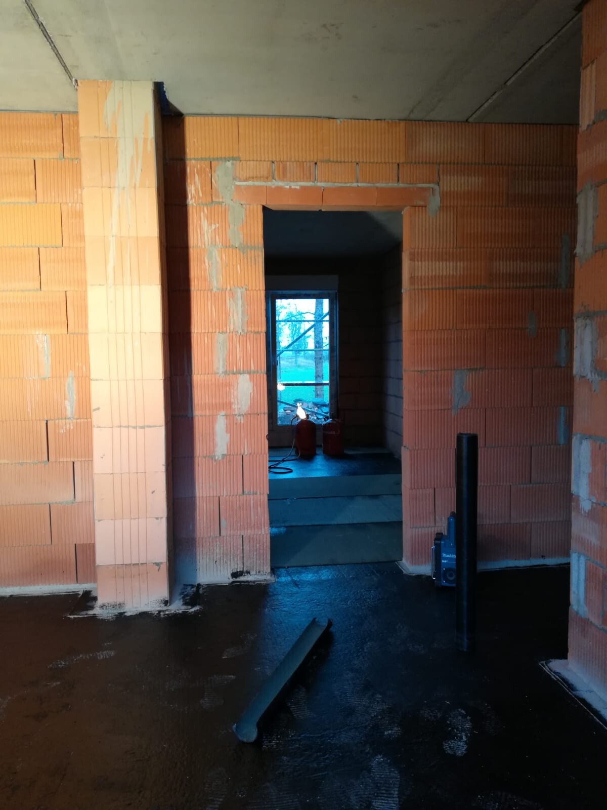 Rohbau-Innenraum mit rotem Ziegelmauerwerk, Türdurchgängen und Bauwerkzeugen.
