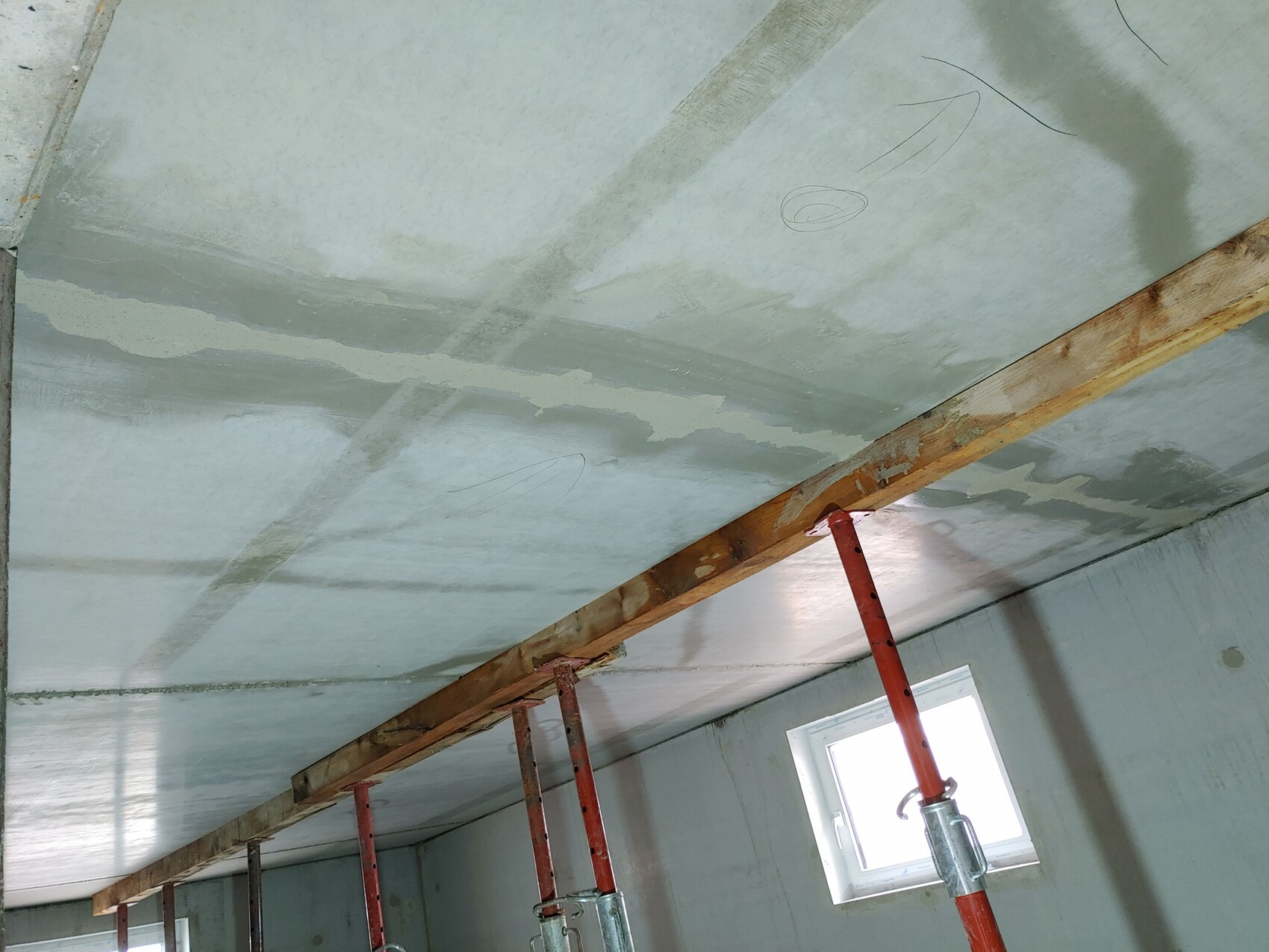 Baustellenraum: Decke mit Spachtelarbeiten, Holzträger und rote Gerüststützen, Fenster im Hintergrund.