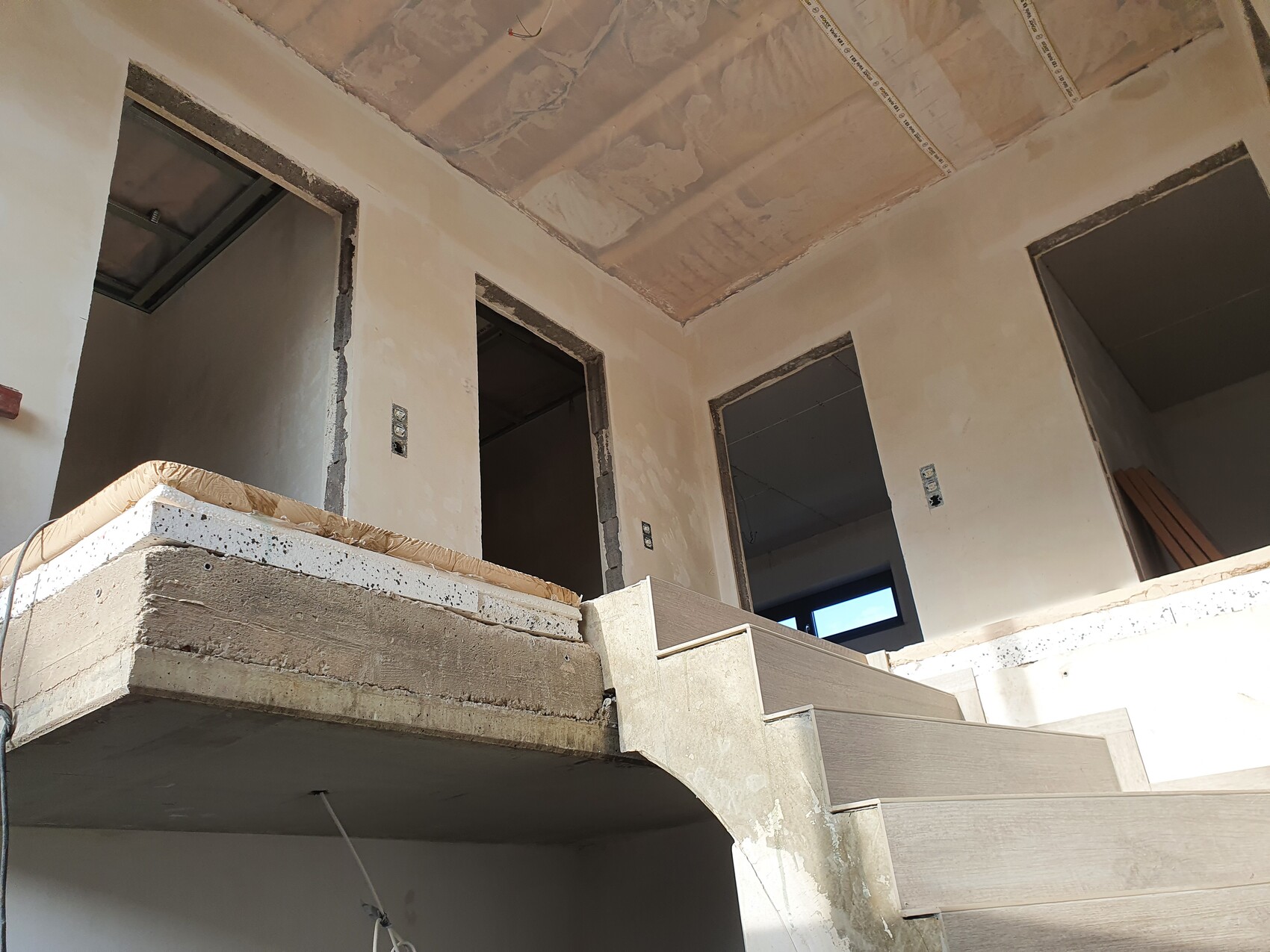 Unfertiger Innenraum eines Gebäudes: Holztreppe, offene Türrahmen und rohe Wände.