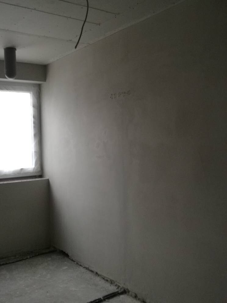 Kleiner, leerer Raum mit grauer Wand, linkes Fenster, sichtbares Rohr an der Decke.