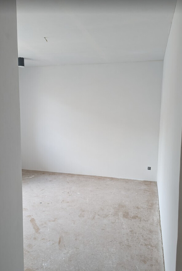 Leerer Innenraum mit weißen Wänden und rohem Betonboden, unmöbliert.