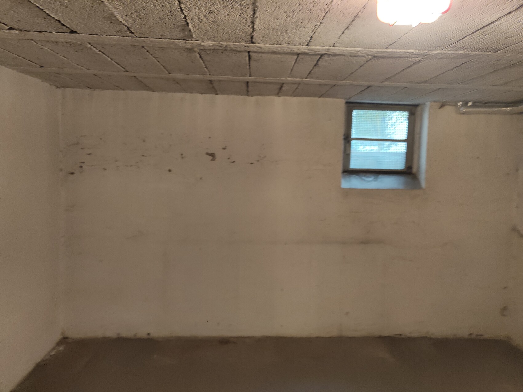 Kellerraum im Rohbau mit Betonwänden, Deckenbalken und kleinem Fenster