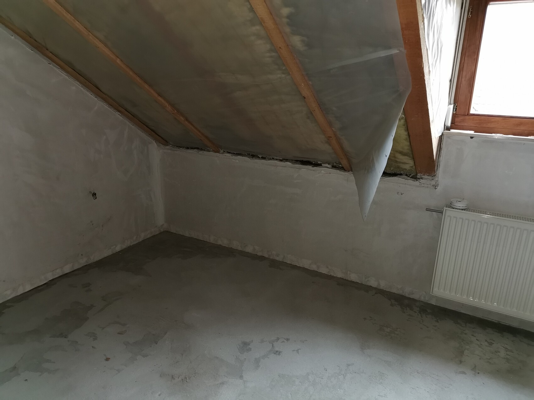 Dachbodenraum mit schräger Decke, Holzbalken, Dämmung und Heizkörper am Fenster.