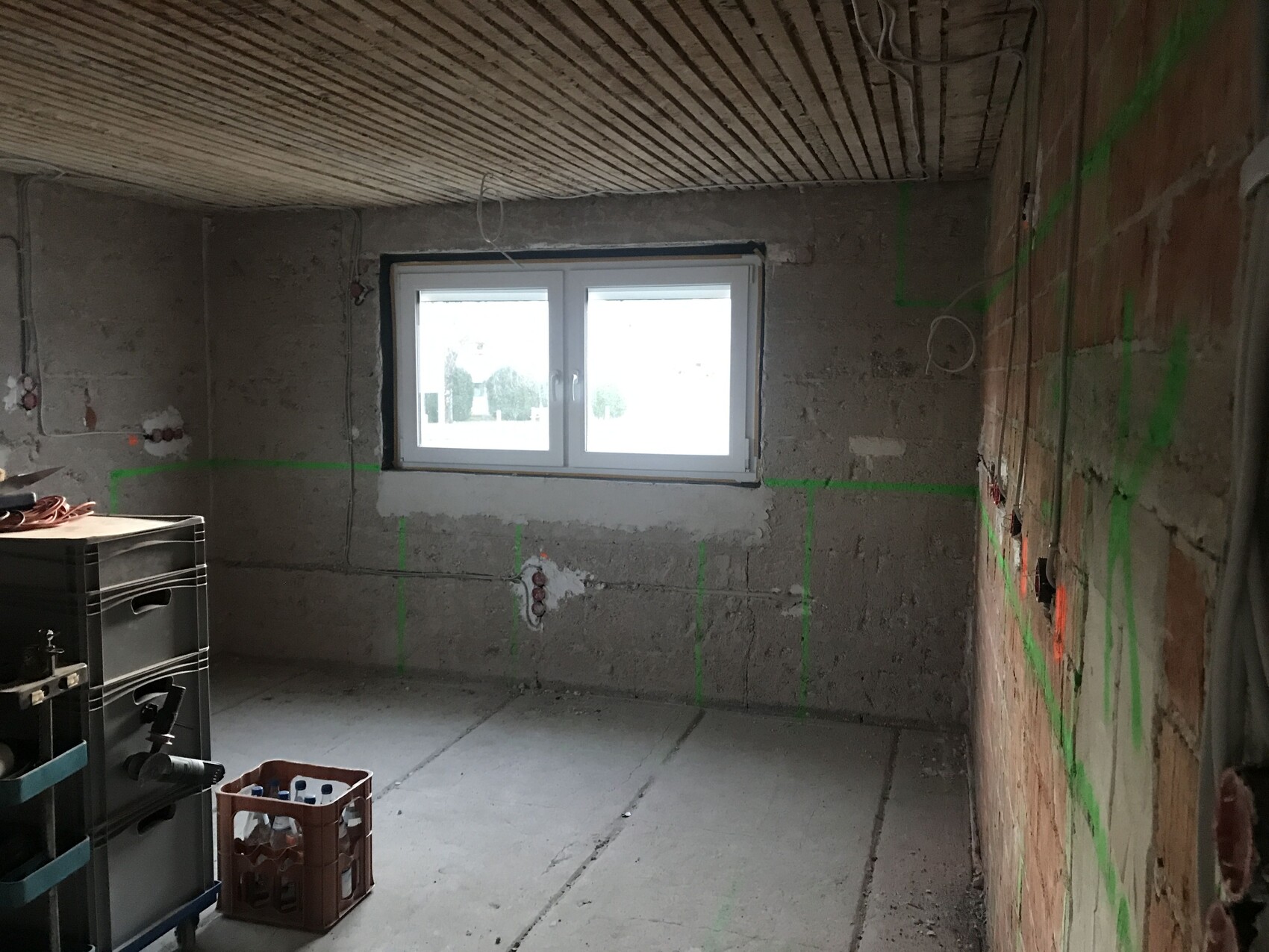 Unbearbeiteter Baustellenraum mit grünen Markierungslinien, Fenster und Kiste mit Flaschen.