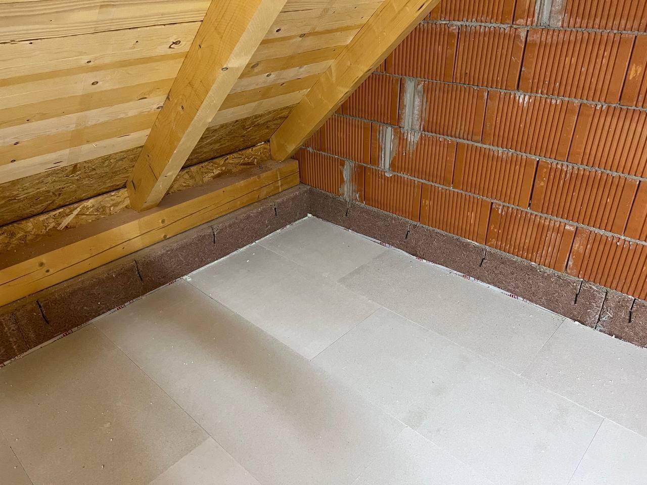 Dachboden-Ecke mit sichtbaren Holzbalken, Ziegelwand und Fliesenboden.