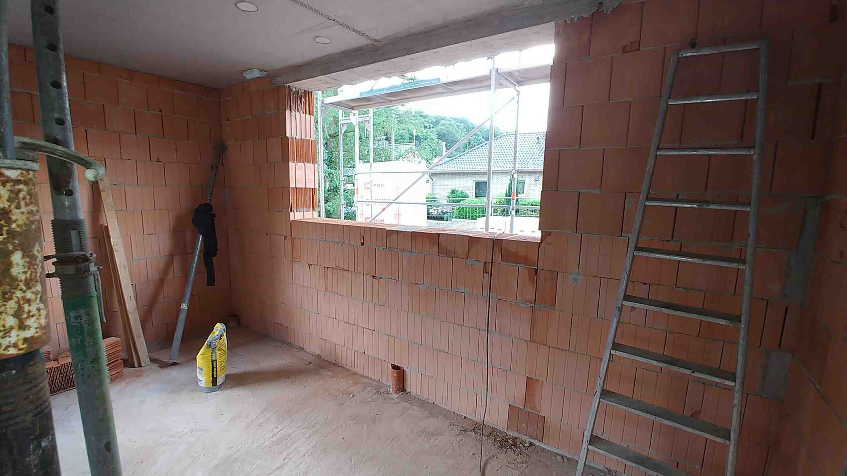 Baustellenraum: Ziegelwände, Leiter, offenes Fenster nach außen, Baugerüst sichtbar.