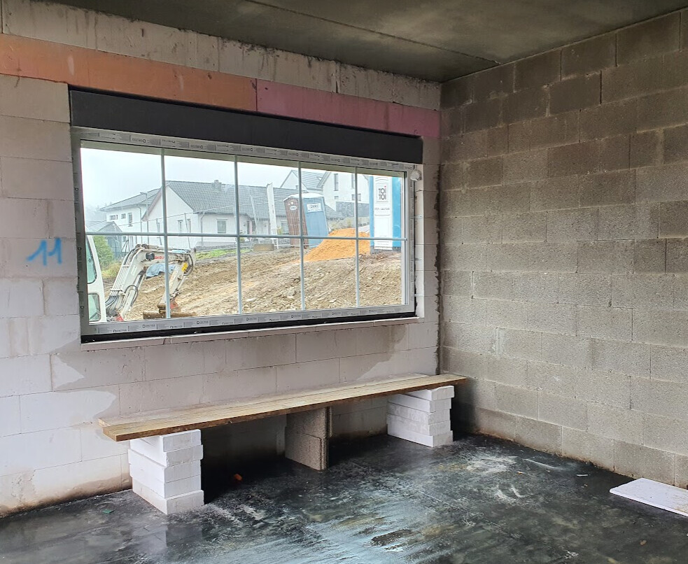Innenraum einer Baustelle: Fensterfront, provisorische Holzbank auf weißen Blöcken, Betonwände
