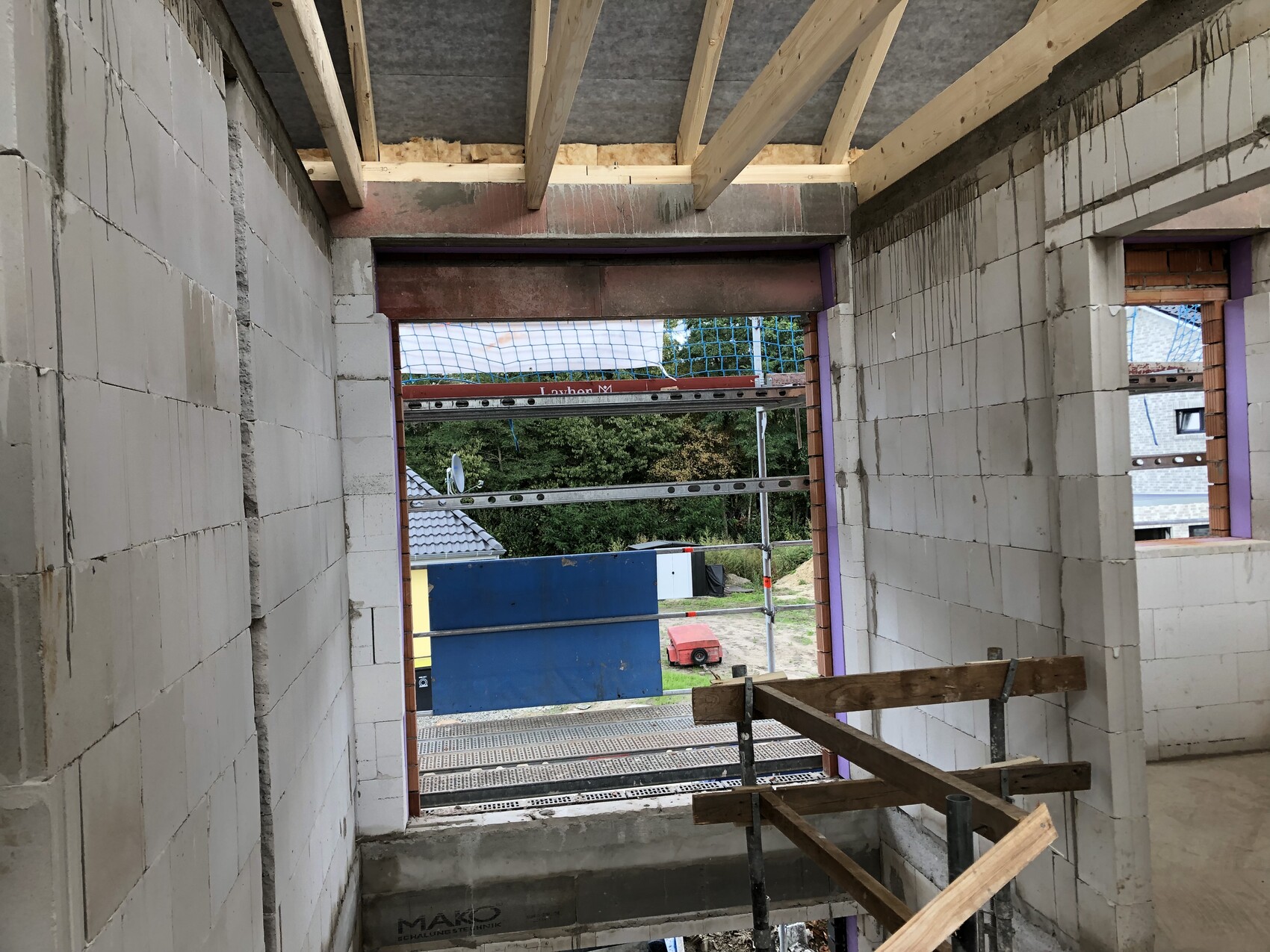 Innenansicht einer Baustelle: Betonblöcke, Holzträgerdecke, Gerüst, offenes Portal nach außen