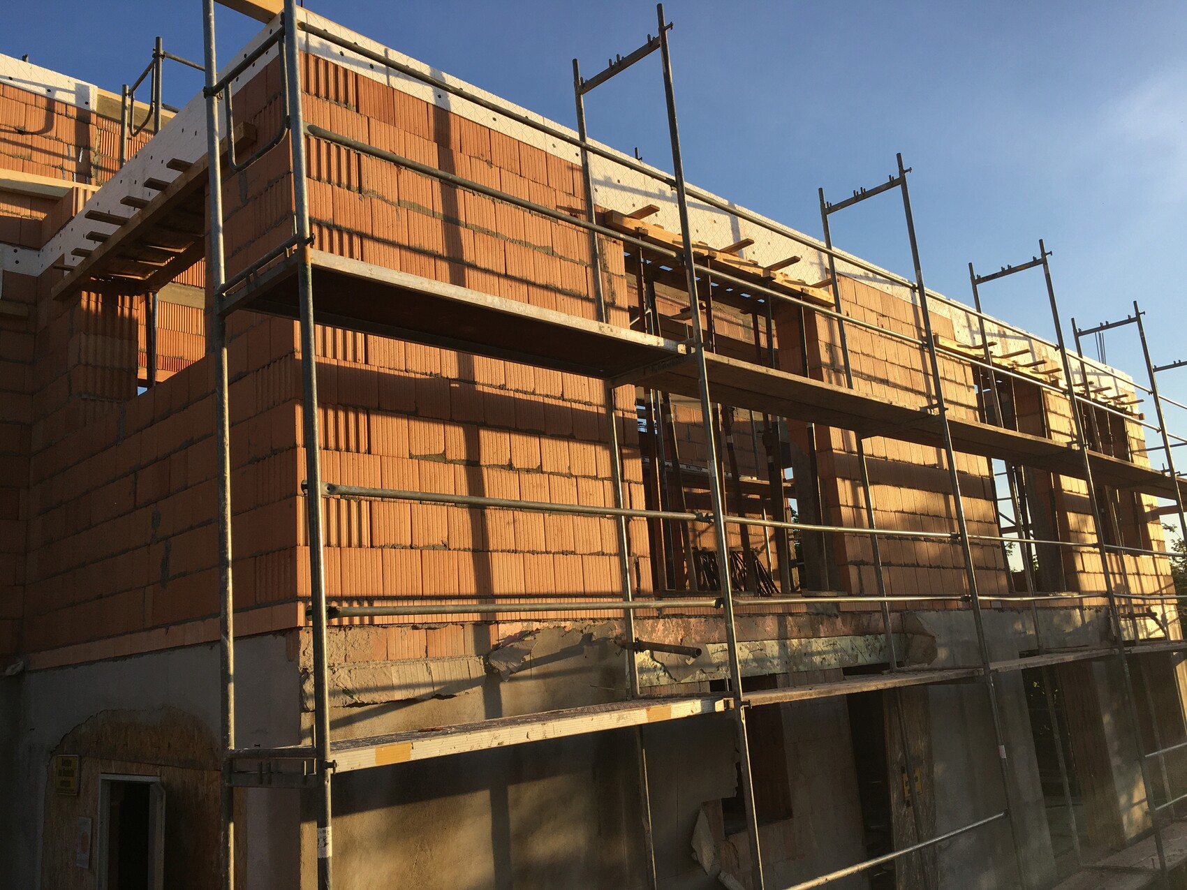Rohbau mit Backsteinmauern, Metallgerüst und Holzbalken an einem Neubau bei Sonnenschein