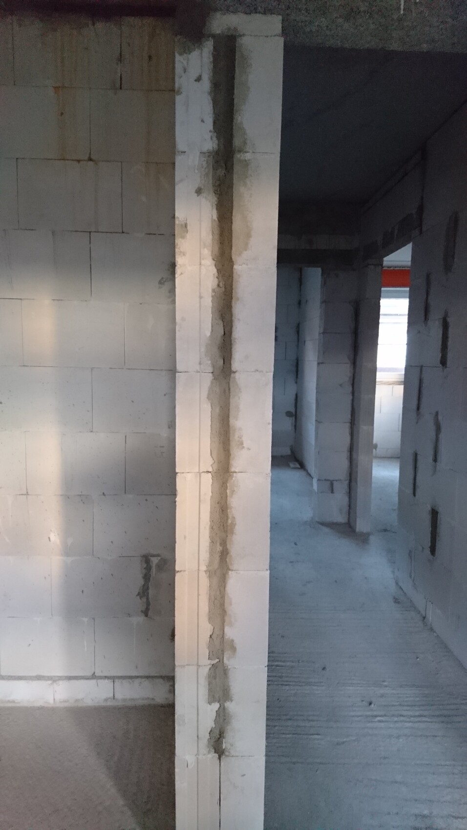 Rohbau-Ansicht: weiße Betonblöcke, rissige Säule, Durchgang in dunklem Flur.