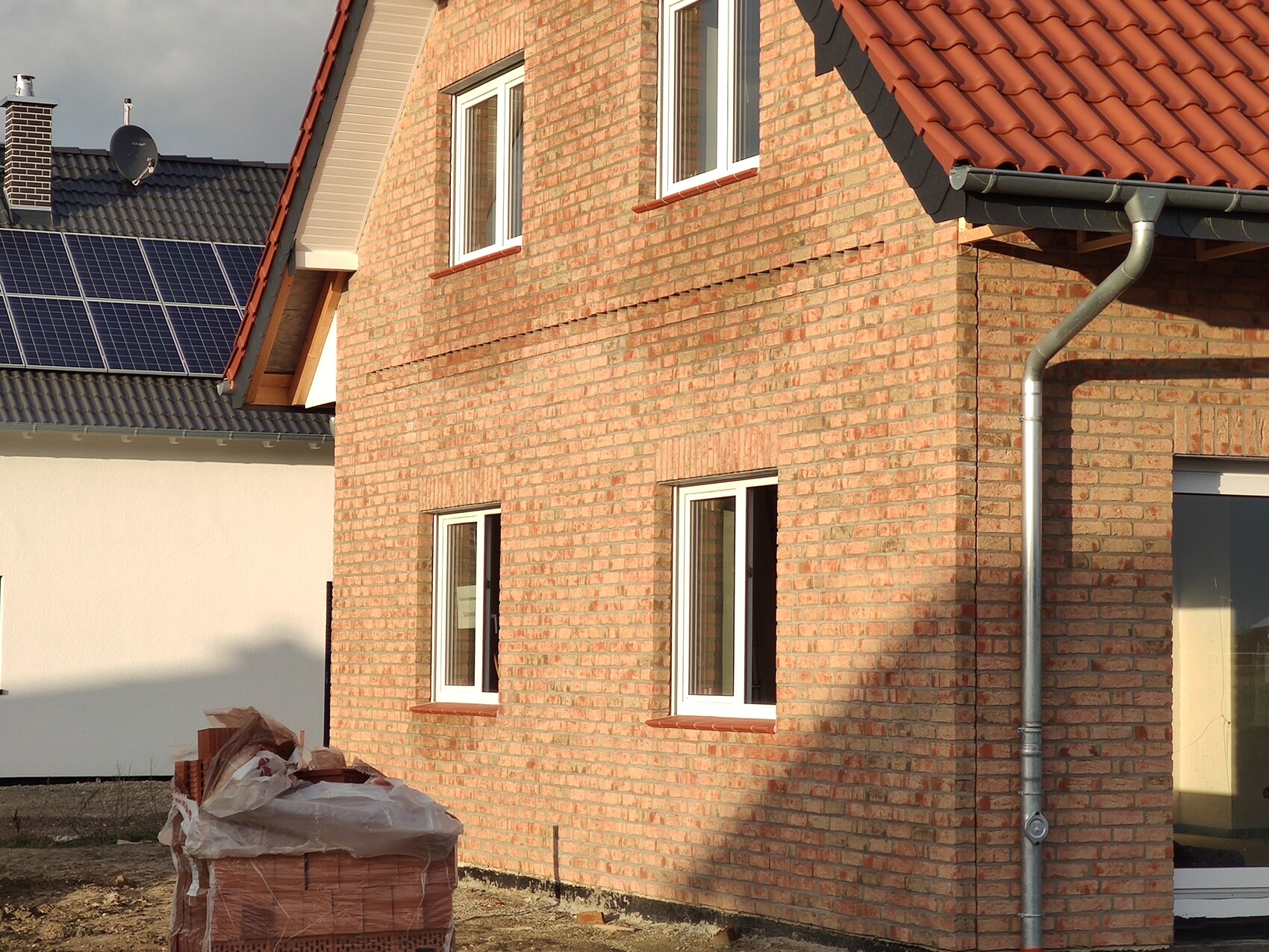 Außenansicht eines unfertigen Ziegelhauses mit Fenstern, Dach und Regenrinne