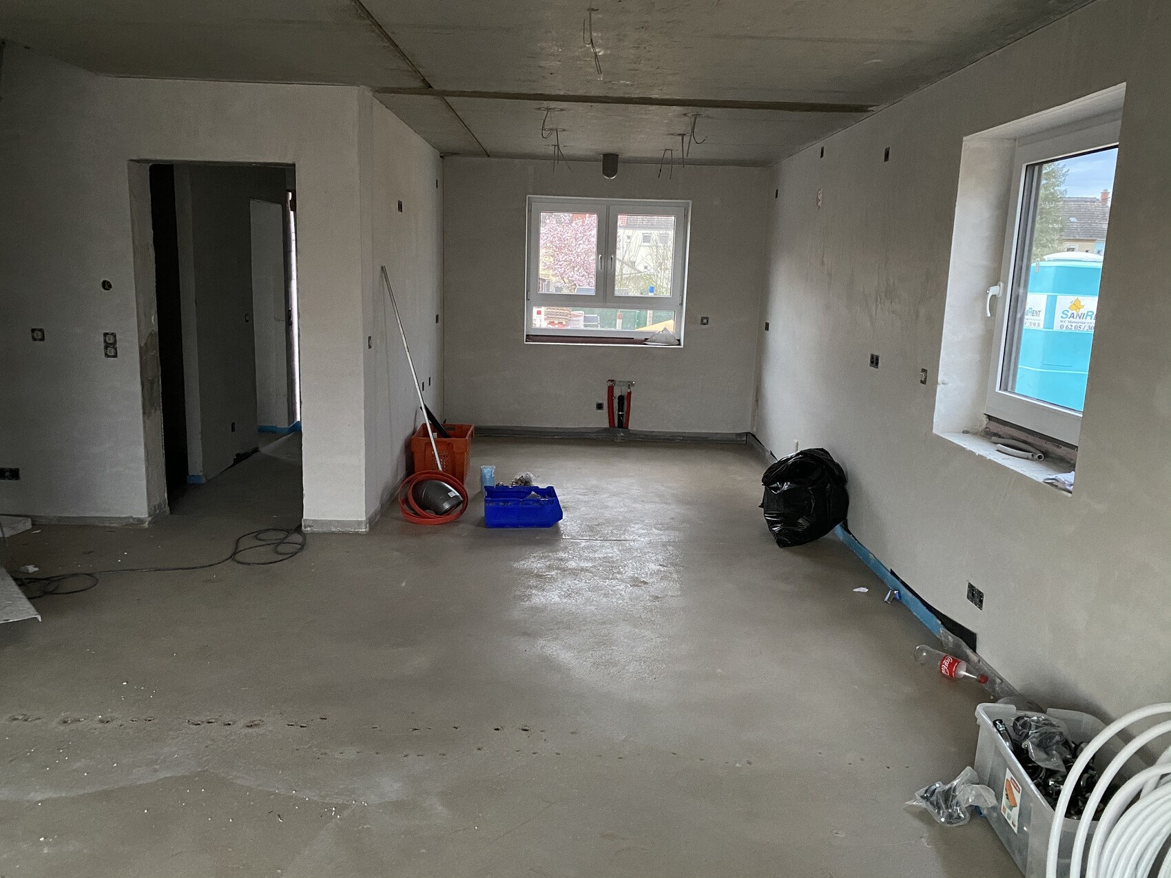 Unrenovierter Innenraum im Rohbau mit Fenster, Werkzeugen, Kabeln und Müllsack.