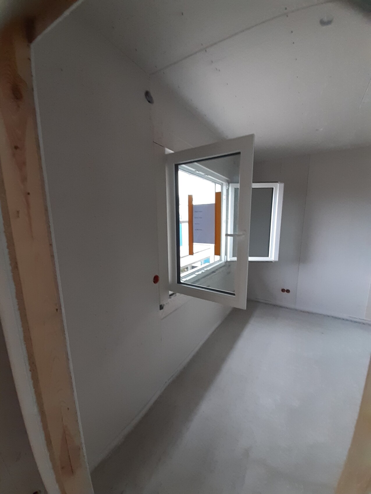 Unfertiger Innenraum mit weißen Wänden, offener Fensterfront und Blick nach außen; Rohbau.