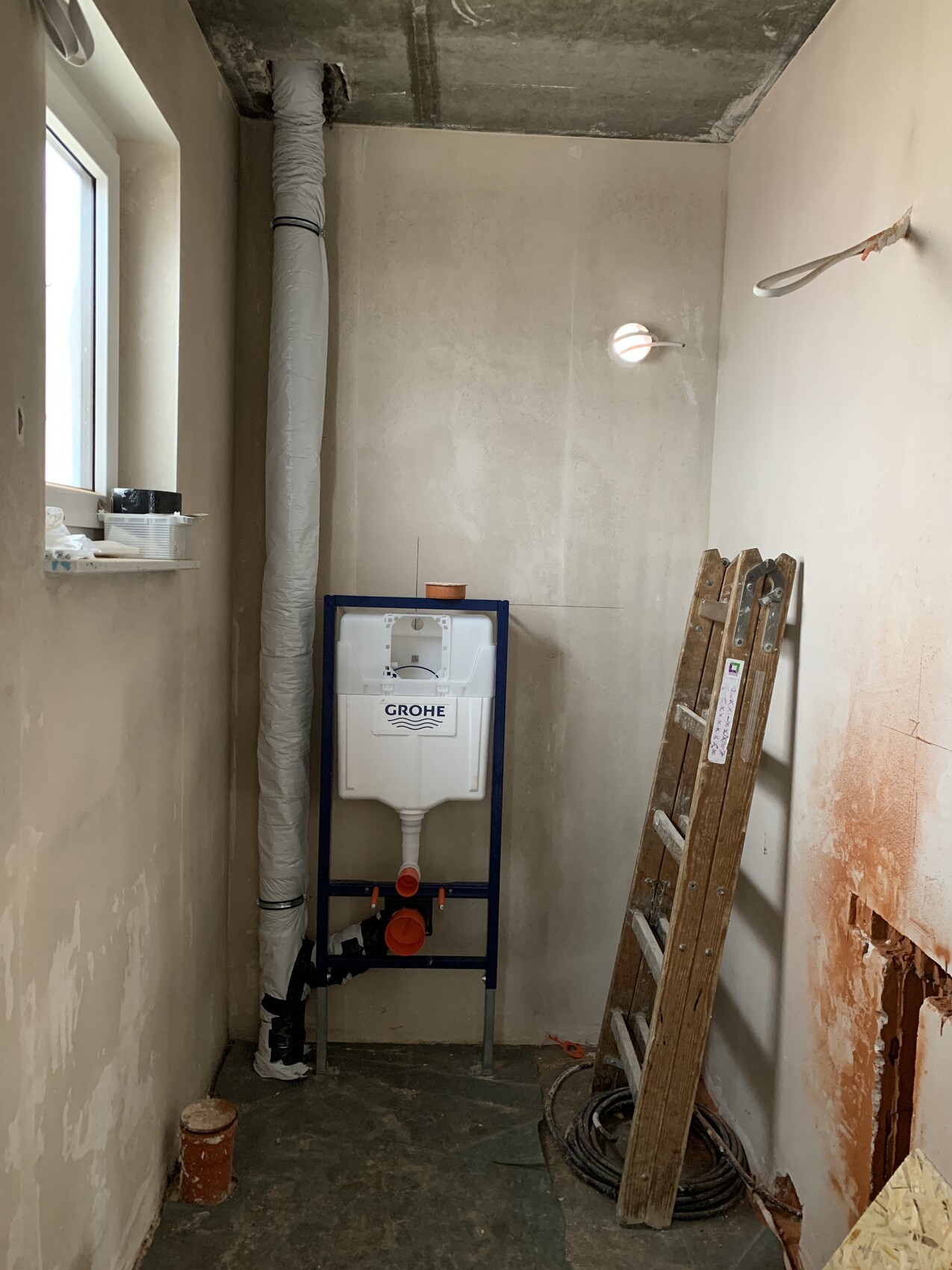 Renovierungsraum mit GROHE-Spülkasten im Rahmen, links isoliertes Rohr, rechts Leiter.