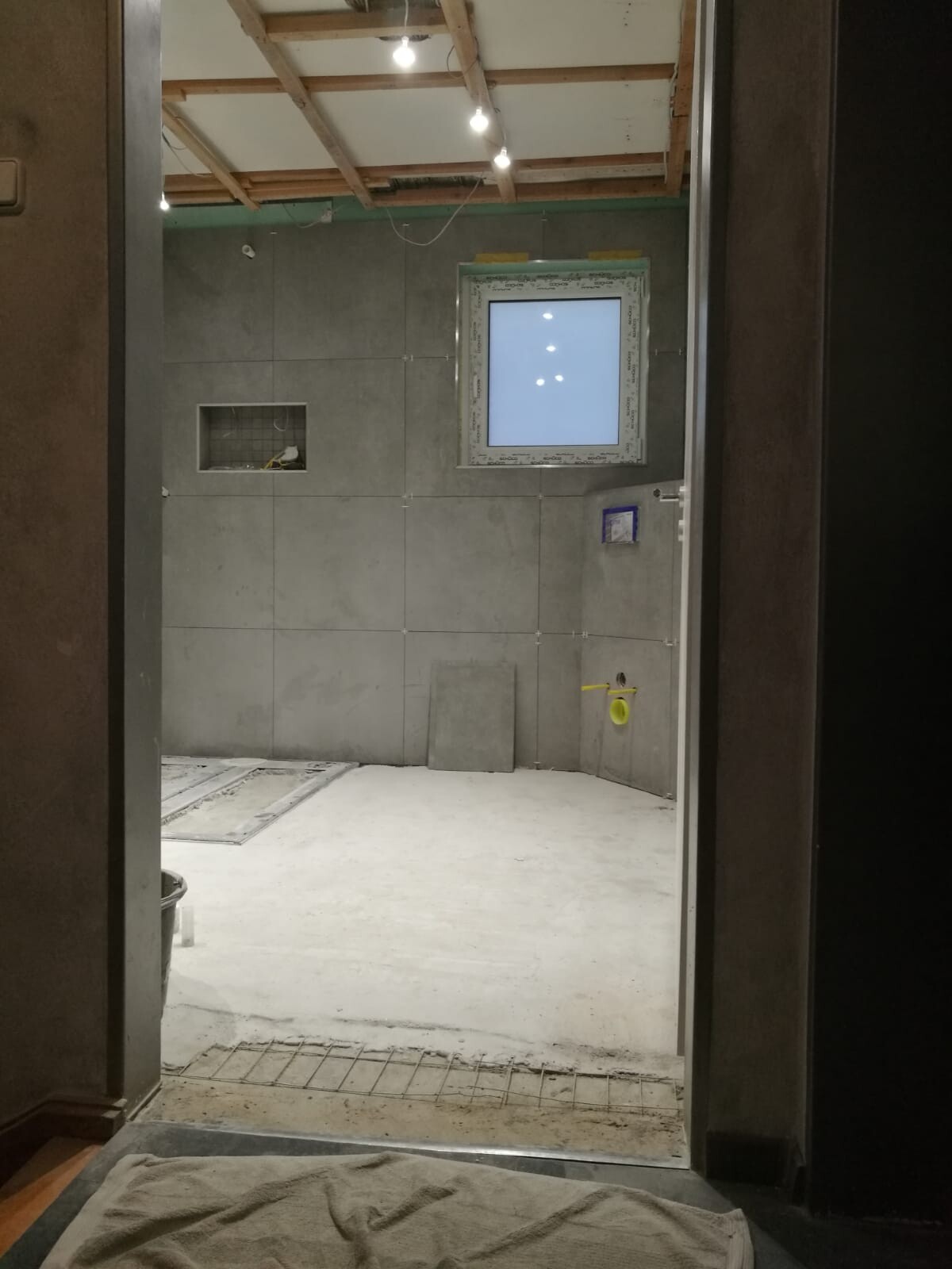 Badezimmer im Bau mit grauen Fliesen, offener Decke und Fenster
