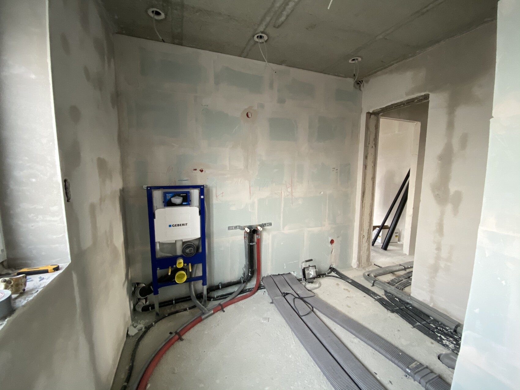 Rohbau-Badezimmer mit Geberit Installationsrahmen, sichtbare Rohre und Kabel auf dem Boden