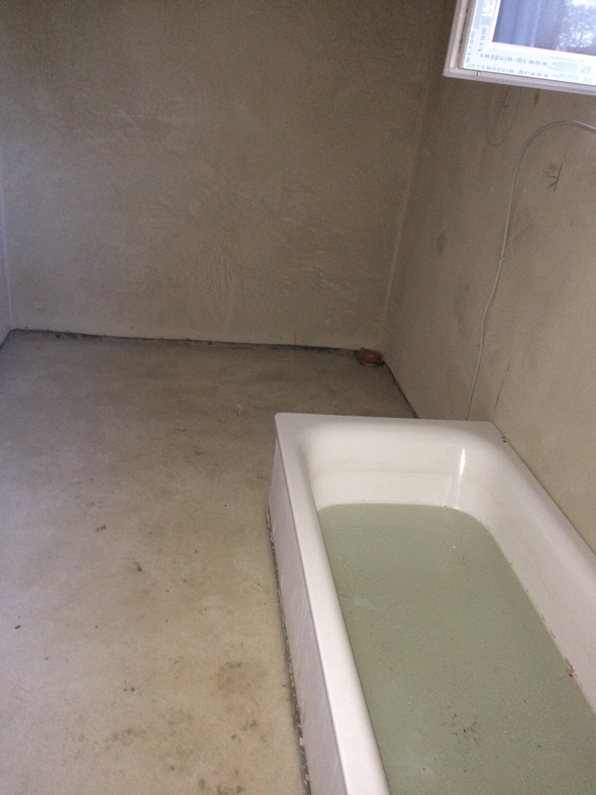 Unfertiges Badezimmer mit roher Wand, Badewanne voll trübem Wasser.