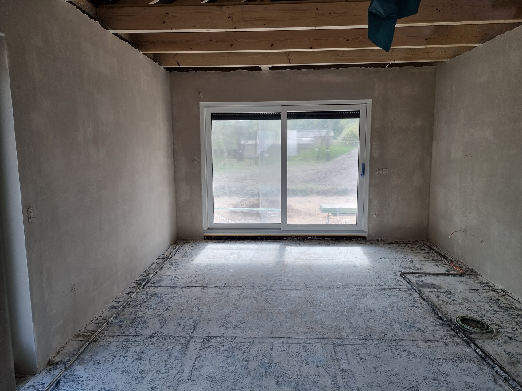 Unfertiger Innenraum mit Betonboden, Rohbau-Wänden und großer Glas-Schiebetür nach draußen.