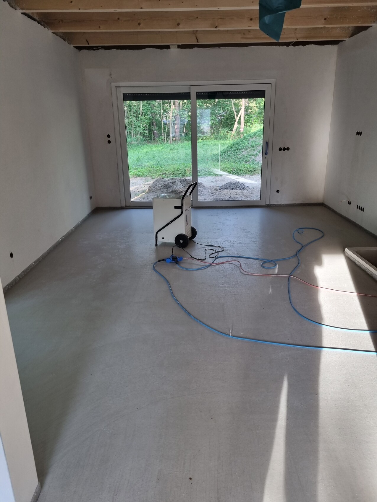 Leerer Renovierungsraum mit großer Glas-Schiebetür, Kabeln und einem mobilen Gerät auf dem Boden