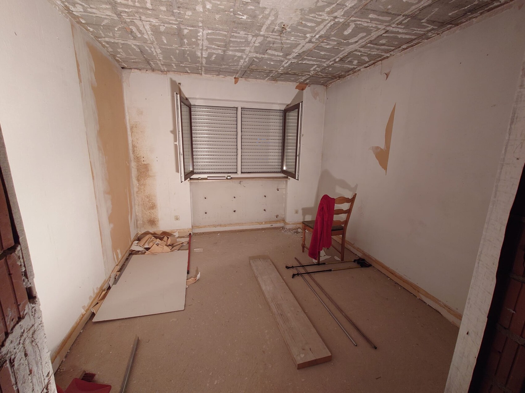 Unfertiges Innenraumzimmer im Bau, Fenster mit Rollladen, Bauwerkzeuge und Stuhl