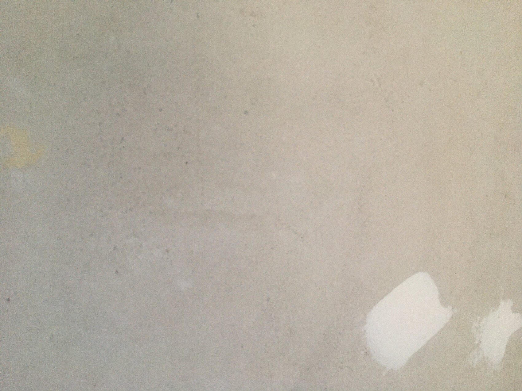 Grau verputzte Wand mit Flecken und abgeblätterte weiße Fläche unten rechts.