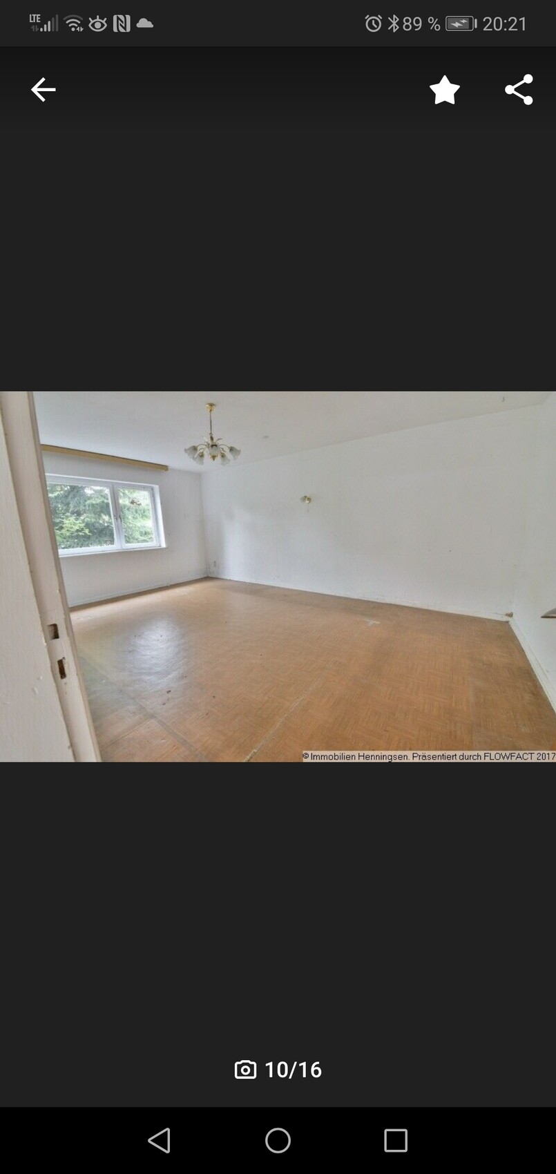 Leeres Wohnzimmer mit Holzparkett, Fenster links und Kronleuchter an der Decke.