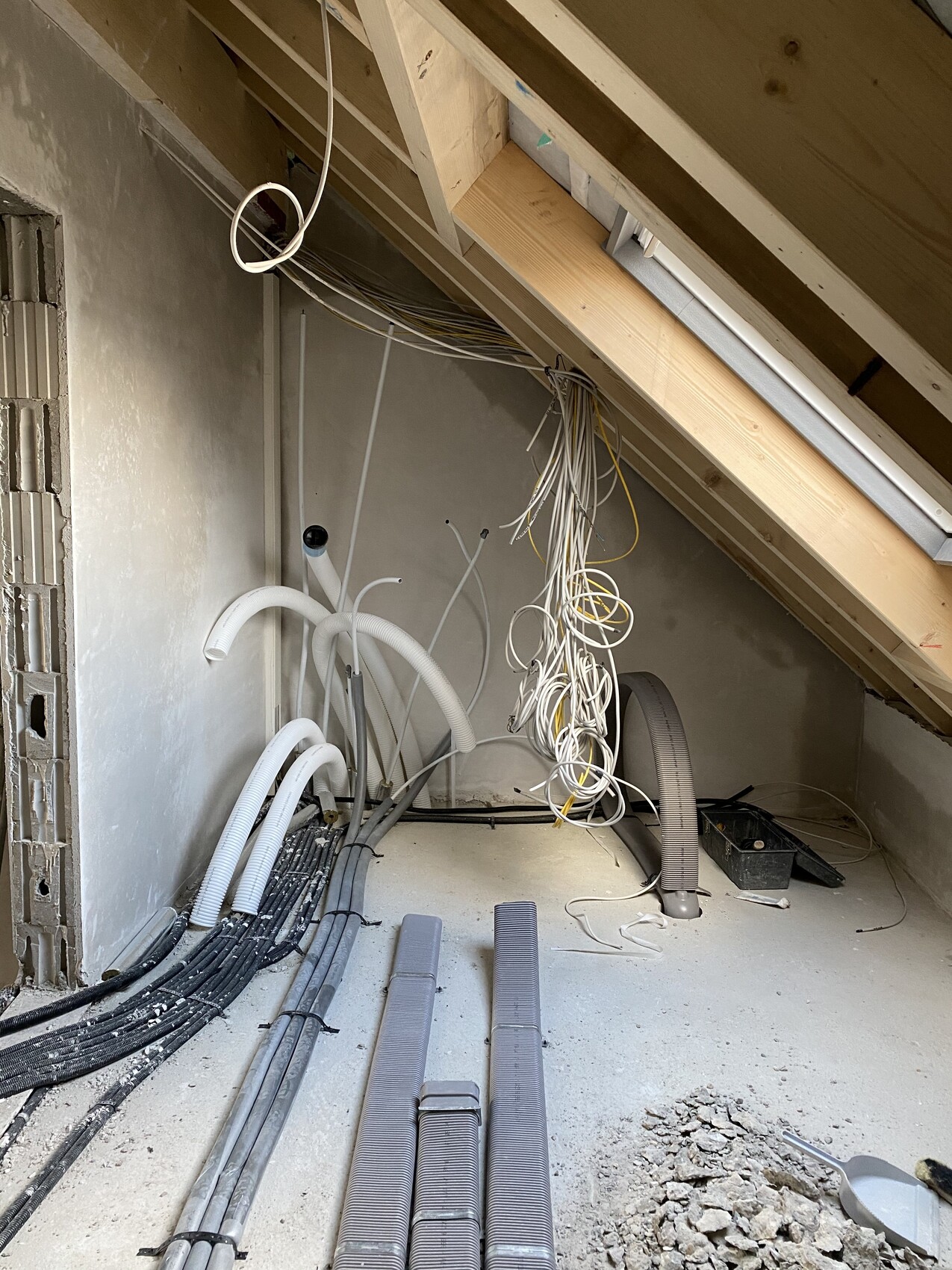Dachboden-Baustelle: lose Kabelstränge, Rohre, Schläuche und Baumaterial liegen verstreut.