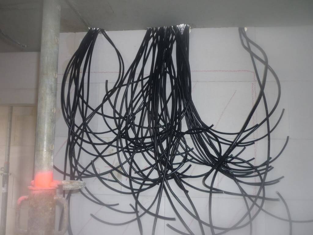 Verhedderte schwarze Kabel hängen von der Decke einer Baustelle; linke Stahlstütze sichtbar.