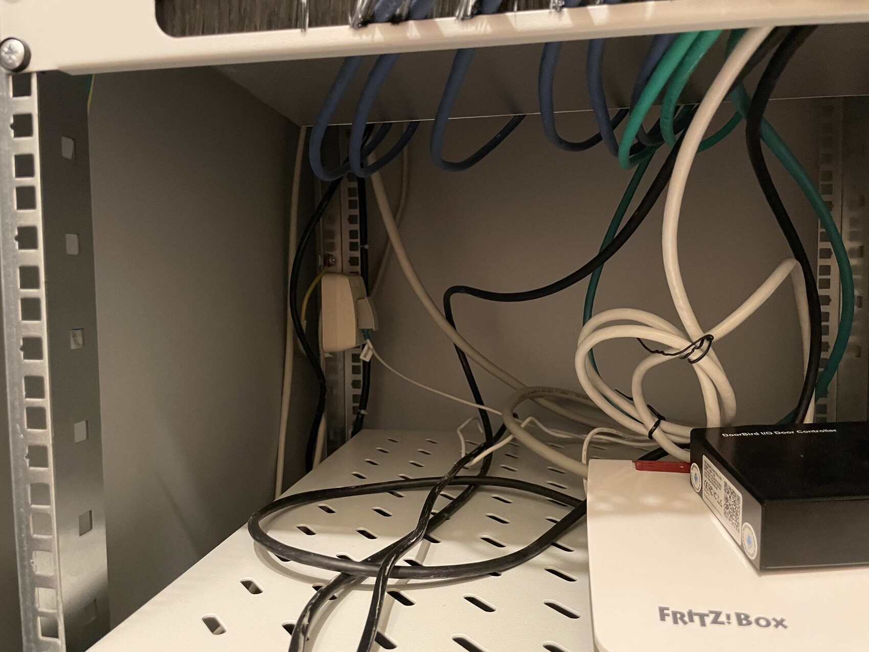 Offener Netzwerkschrank mit vielen Kabeln, blauen Ethernetkabeln und einer FRITZ!Box-Box.