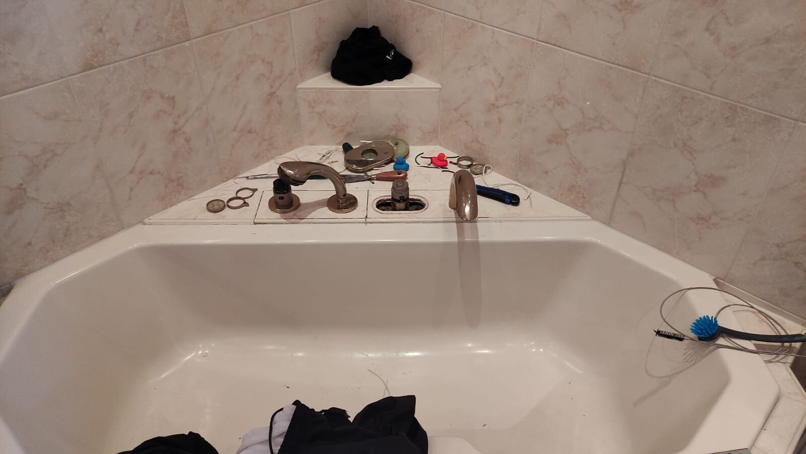 Badewanne mit verstreuten Sanitärteilen, Ringen und Werkzeugen; blaue Bürste am Rand.