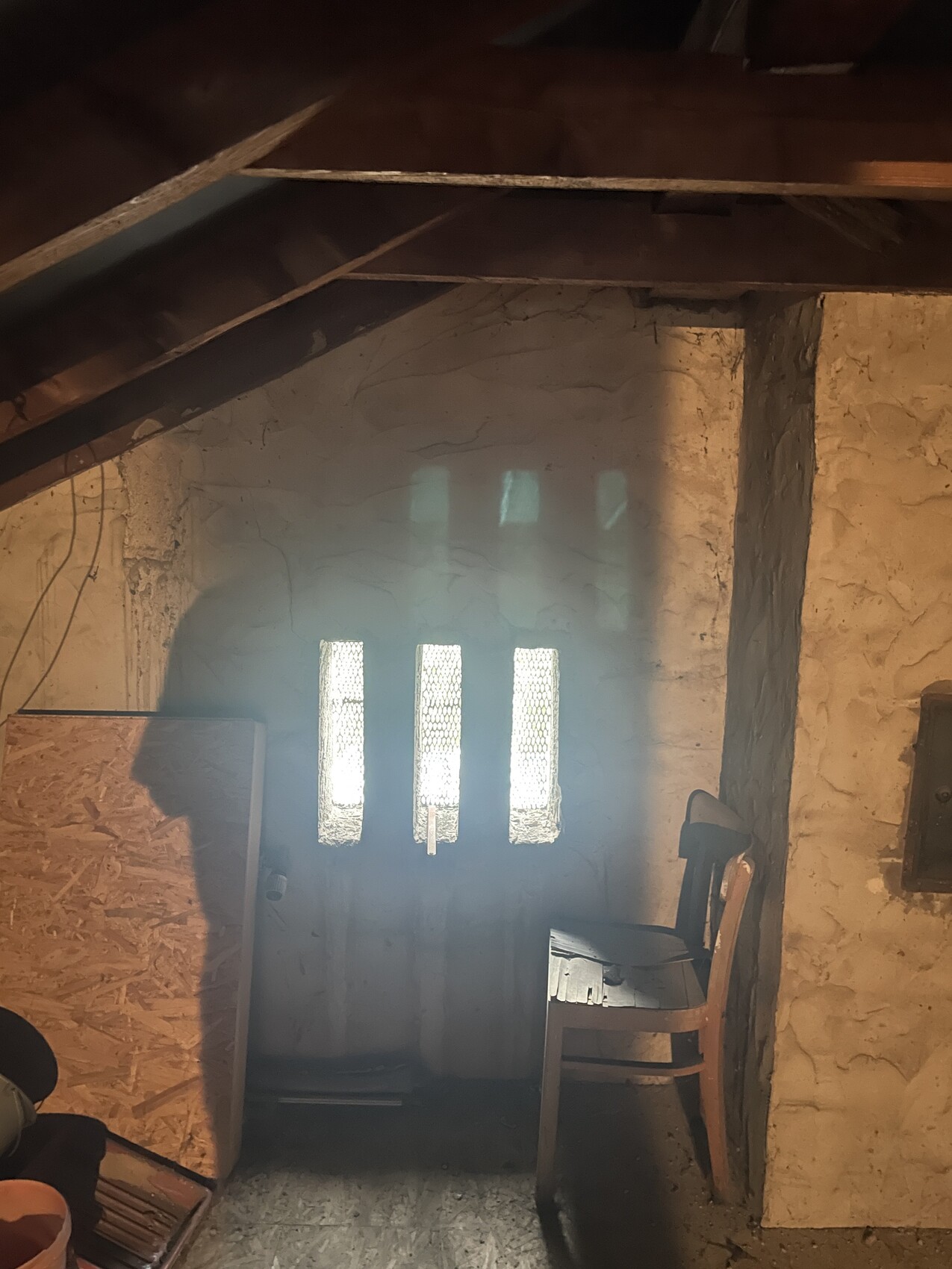 Dachboden mit Holzbalken, Tür mit vier schmalen Glasfenstern, Stuhl rechts.