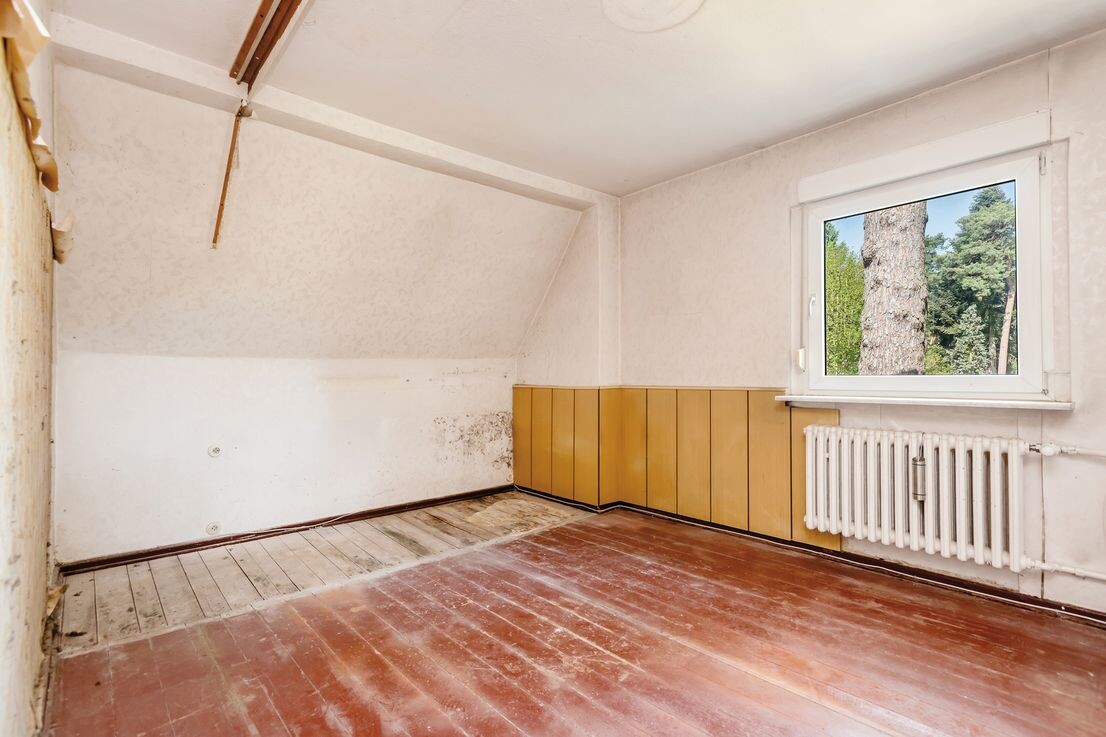 Unrenovierter Dachgeschoss-Innenraum mit Fenster, Heizkörper und Holzboden