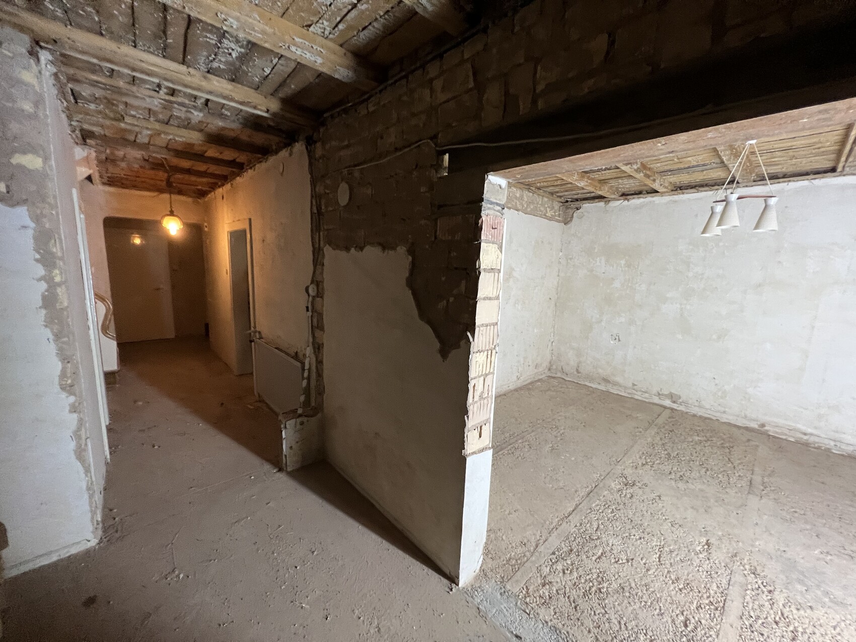 Keller mit Holzbalkendecke, halbfertige Wände; rechts leeres Zimmer mit Dreifachlampe.